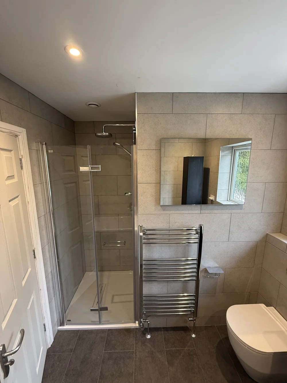 Stone-tiled family bathroom with hinged glass shower enclosure and chrome towel rail — bathroom installation