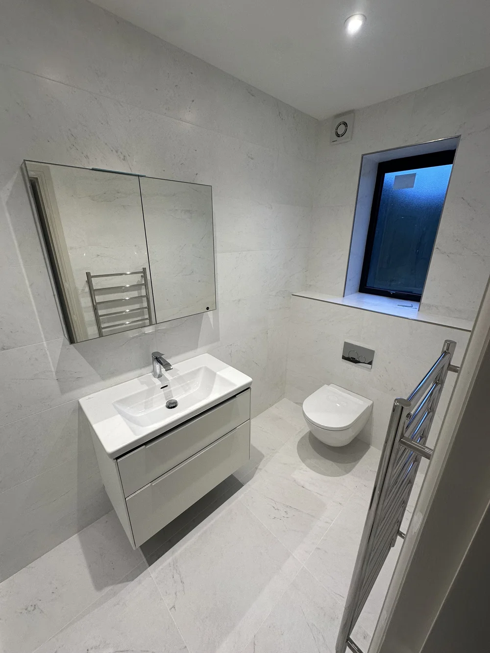 White marble ensuite with wall-hung vanity, mirrored cabinet and back-to-wall WC