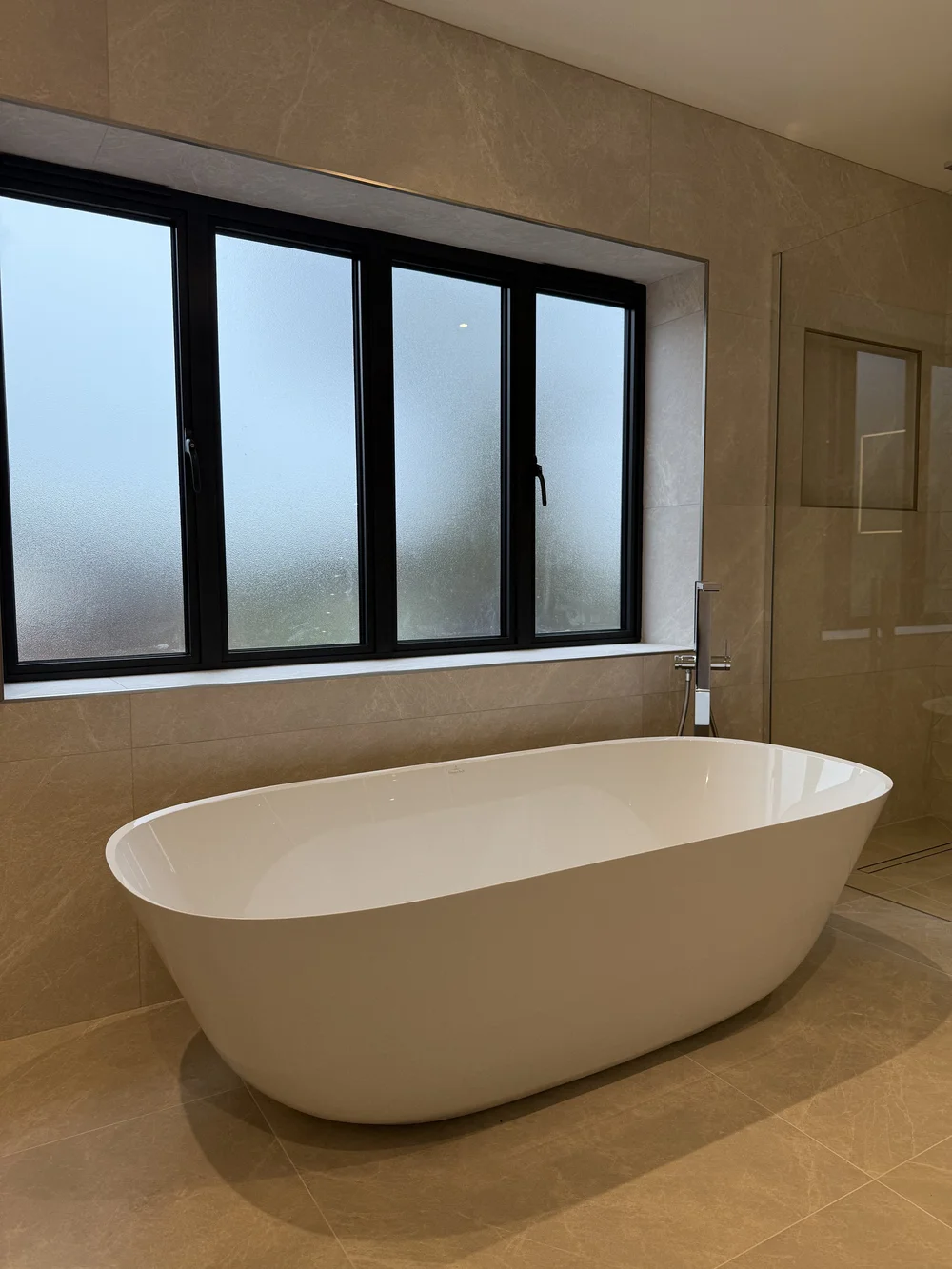 Freestanding bath under crittall window in stone-tiled master bathroom