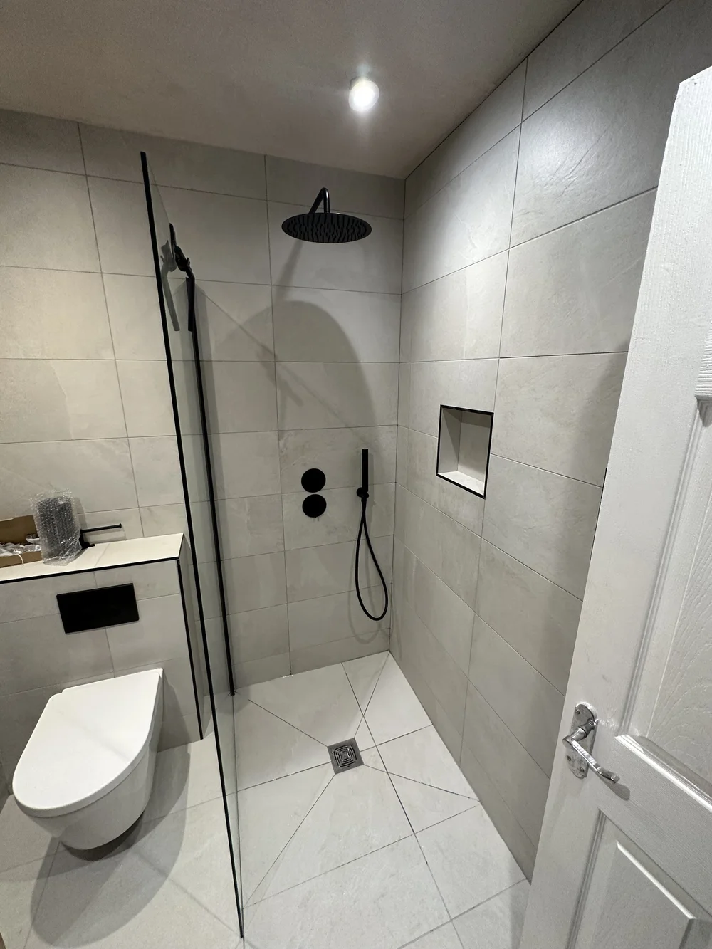 Stone-tiled walk-in shower with matte black rainfall head and recessed niche — wet room